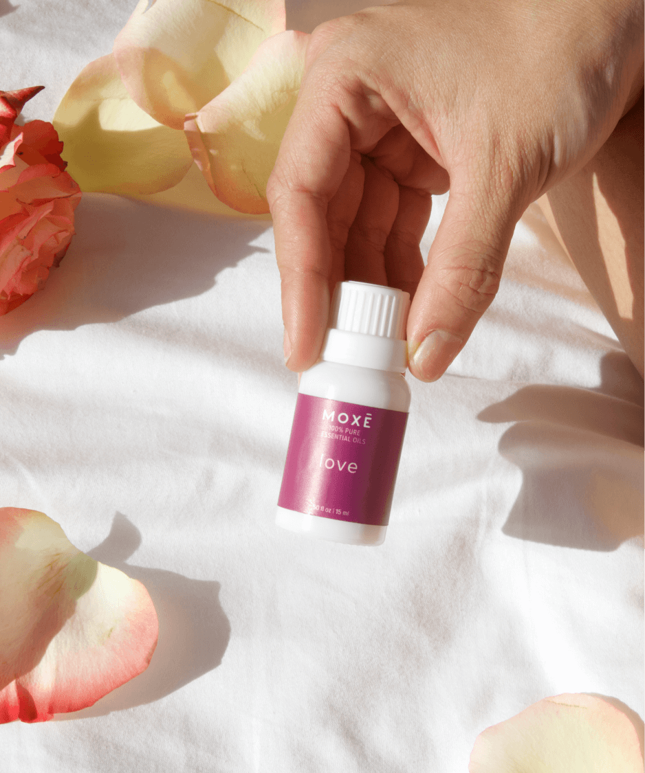 Hand holding MOXE Love essential oil with rose petals