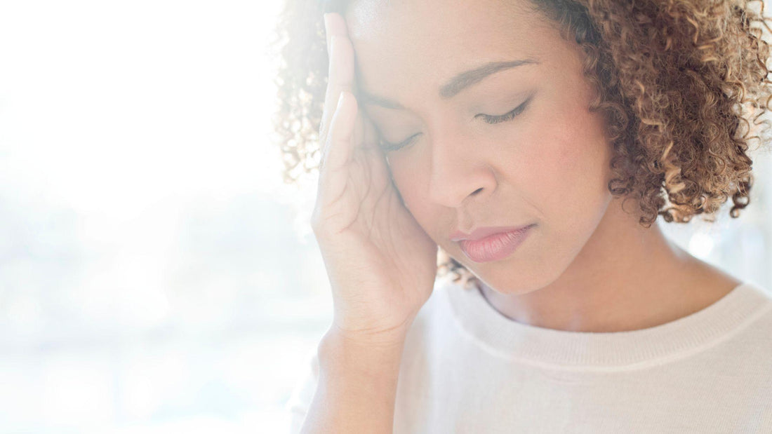 Woman suffering from a migraine holding left temple in discomfort