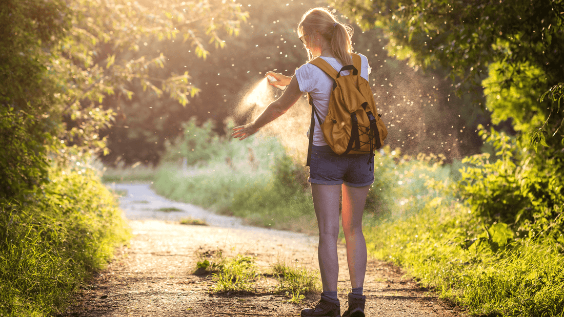 Woman on trail spraying insect repellent onto left arm