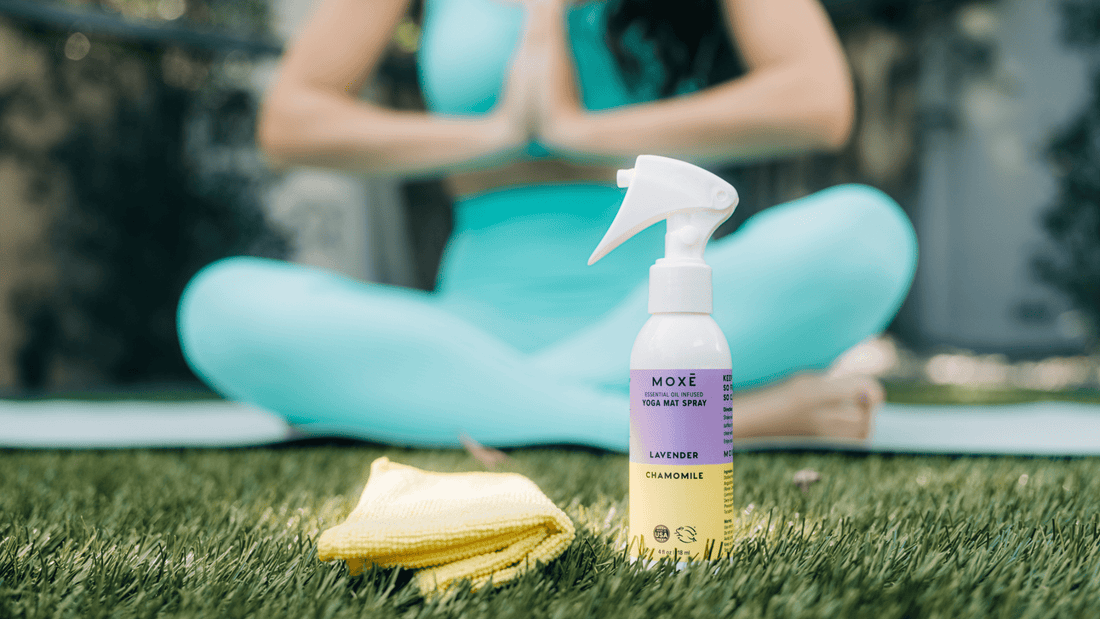 MOXĒ Lavender Chamomile Yoga Mat Spray sitting in the grass in front of a woman doing yoga