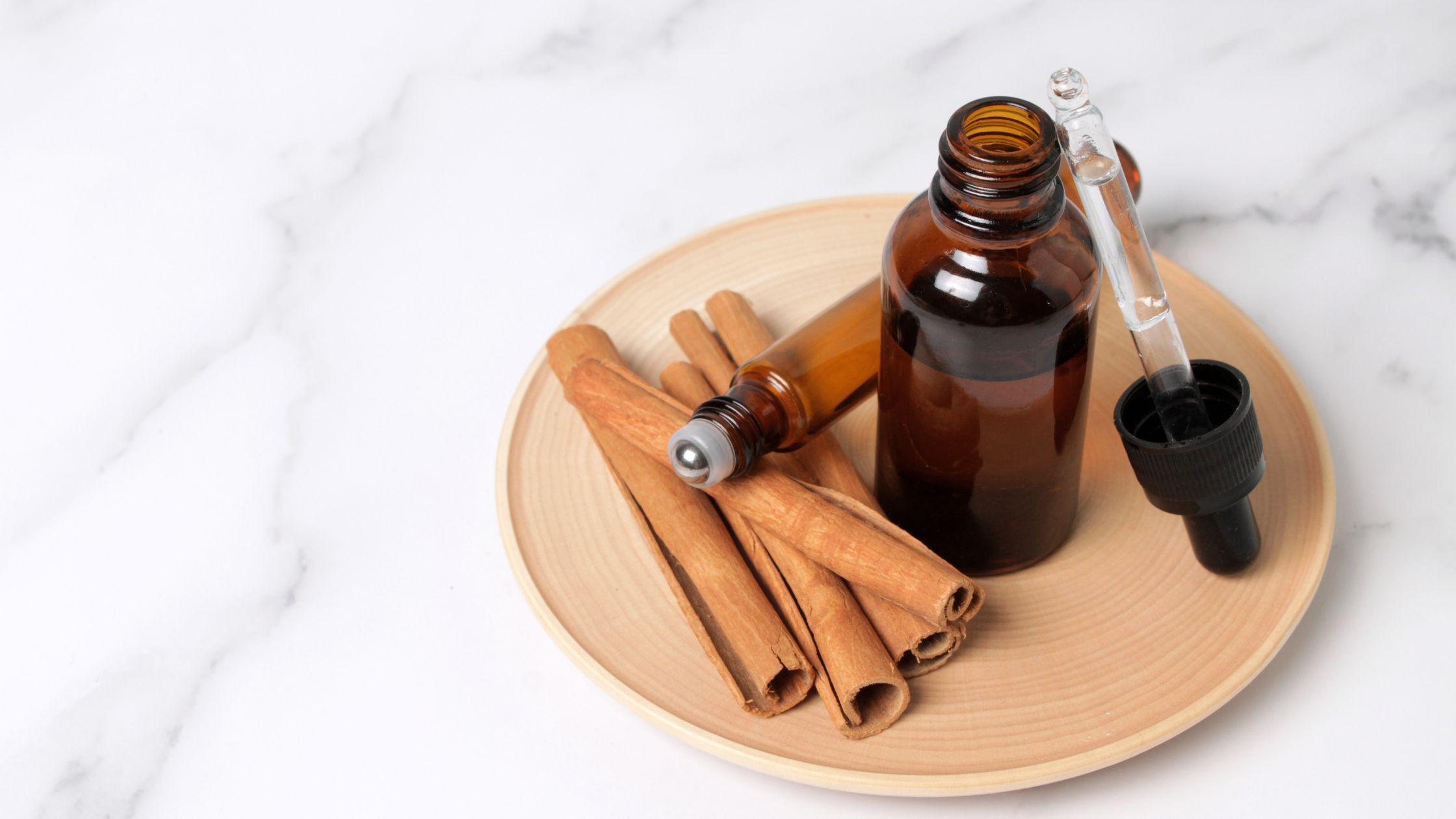 Cinnamon stick sitting next to an open essential oil bottle and dropper