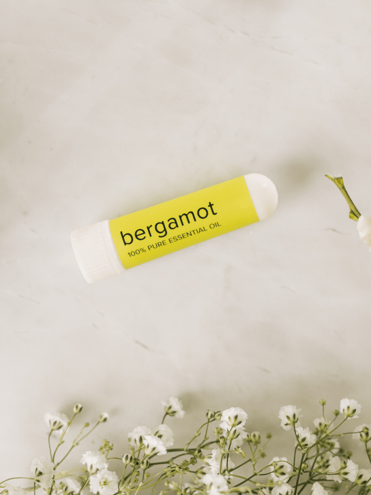 MOXĒ Bergamot Aromatherapy Nasal Inhaler laying on counter surrounded by flowers