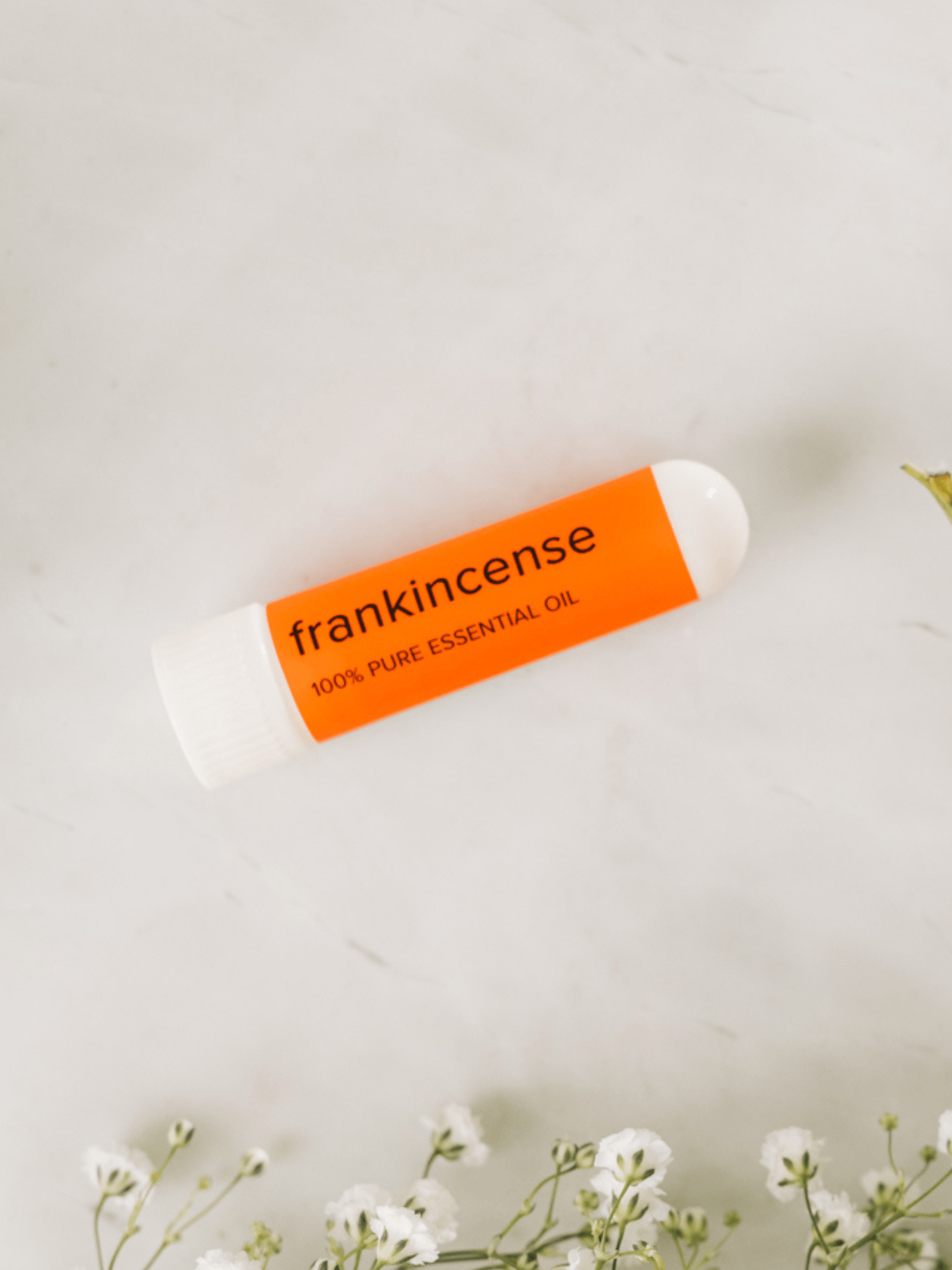 MOXĒ Frankincense Aromatherapy Nasal Inhaler laying on counter surrounded by flowers