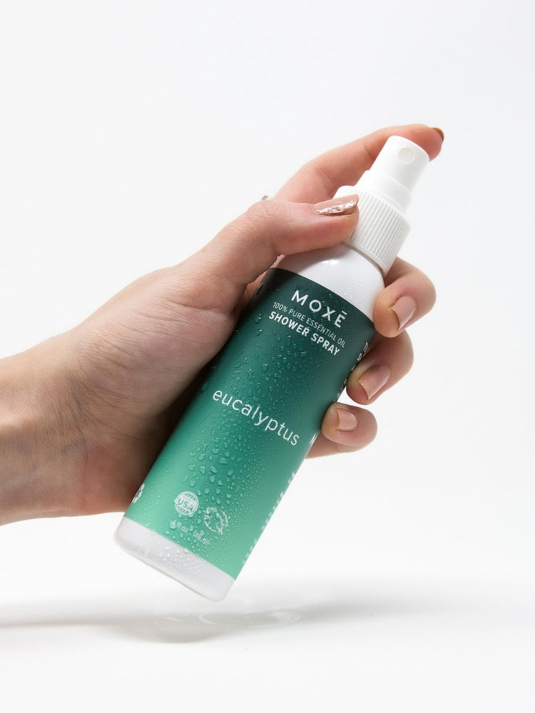 White bottle MOXĒ Eucalyptus Shower Spray with a hand holding it