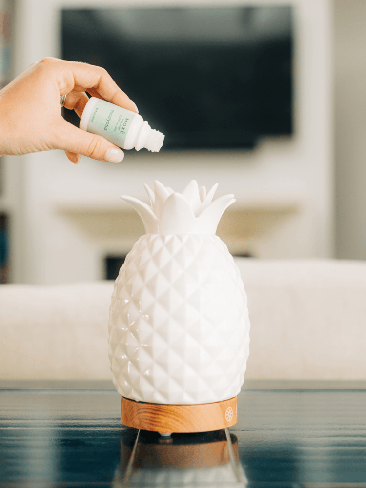Hand pouring MOXE Eucalyptus Essential Oil into pineapple-shaped diffuser