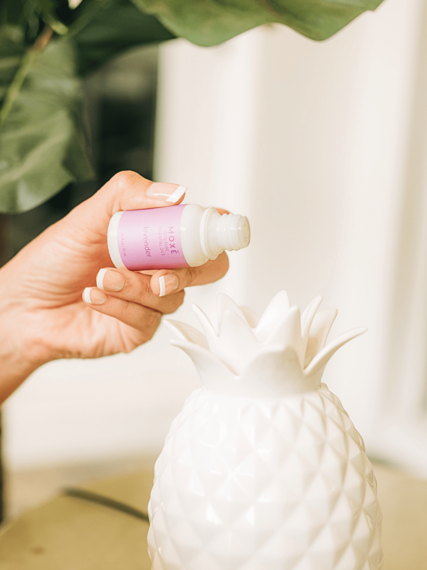 Hand pouring MOXĒ Lavender Essential Oil into pineapple shaped diffuser