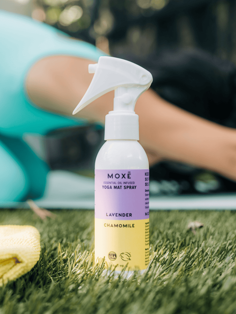 MOXĒ Lavender Chamomile Yoga Mat Spray sitting in the grass in front of woman doing yoga