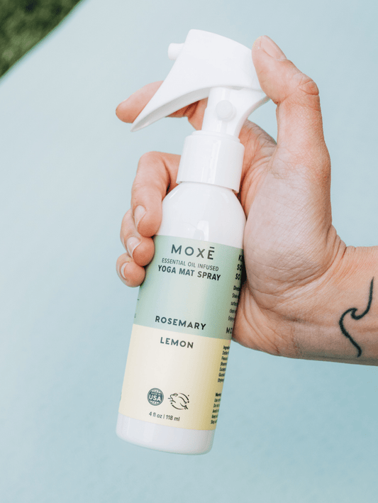 Hand holding the MOXĒ Rosemary Lemon Yoga Mat Spray