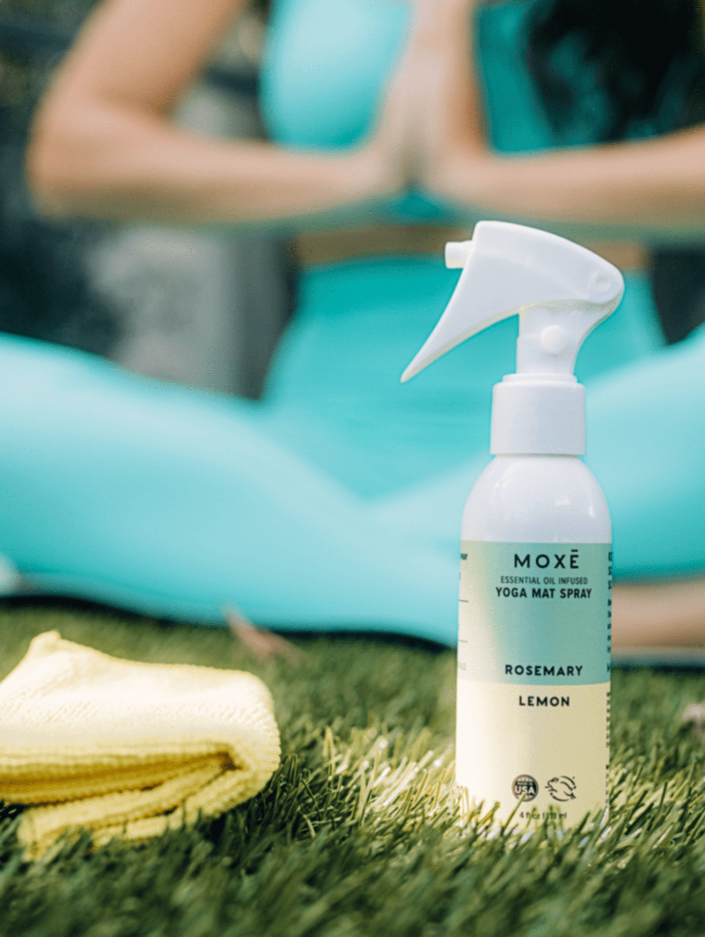 MOXĒ Rosemary Lemon Yoga Mat Spray sitting in grass with woman doing yoga